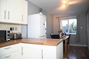 a kitchen with white cabinets and a wooden counter top at 2ndHomeStays- Willenhall-A Serene 3 Bed House with a Garden View-Suitable for Contractors and Families-Sleeps 9 - 7 mins to J10 M6 and 21 mins to Birmingham in Willenhall