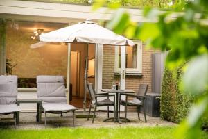 una mesa con sillas y una sombrilla en el patio en Heerlijk vakantiehuisje op rustig Natuurpark en Otterlo