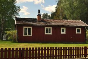 una casa roja con una valla delante en Stuga i vassemåla, en Vimmerby