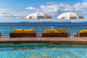 een zwembad met twee parasols en stoelen naast de oceaan bij Hôtel Le Bailli De Suffren in Rayol-Canadel-sur-Mer