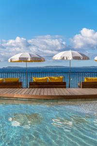 een zwembad met twee parasols en de oceaan bij Hôtel Le Bailli De Suffren in Rayol-Canadel-sur-Mer