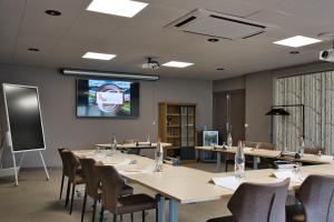 a conference room with tables and chairs and a screen at Hôtel du Golf de l'Ailette, The Originals Relais (Qualys-Hotel) in Chamouille