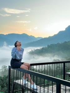 uma mulher sentada numa varanda com vista para as montanhas em Leaf Olu Ella em Yatiyantota