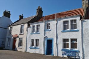 ein weißes Haus mit einer blauen Tür und einer Bank in der Unterkunft Sand And Sea Cottage- lovely family home Crail in Crail