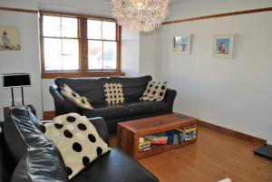 ein Wohnzimmer mit einer schwarzen Couch und einem Tisch in der Unterkunft Sand And Sea Cottage- lovely family home Crail in Crail