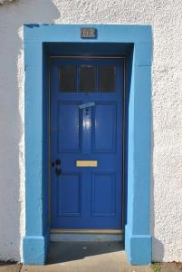 a blue door in a white building with at Sand And Sea Cottage- lovely family home Crail in Crail