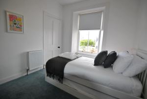 a white bedroom with a bed with pillows and a window at Creel Cottage- stylish cottage near the sea in Anstruther