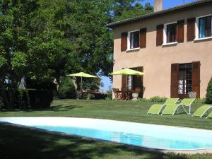 una piscina di fronte a una casa con sedie e ombrelloni di Coumassous a Arricau-Bordes