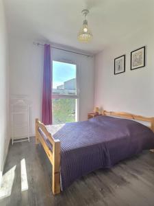 1 dormitorio con cama con colcha púrpura y ventana en Confortable pavillon climatisé à 500m de la mer en Sérignan