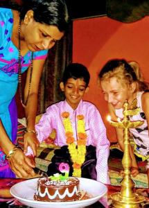 a woman cutting into a cake with a child at Cockerel Homestay - Traditional Beach Village - Goa in Canacona