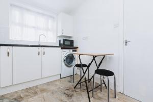 a white kitchen with a washing machine and a table at The Dahlia Rooms - free parking & wifi in Barking