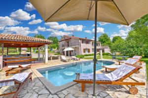 a pool with chairs and an umbrella next to a house at House Marica 1887 in Tinjan