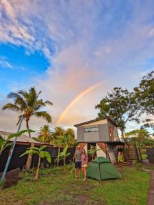 a woman standing in front of a house with a rainbow at Moehiva Camping Rapa Nui in Hanga Roa
