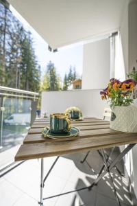 a wooden table with two cups and a vase of flowers at Apartament Black Diamond in Szklarska Poręba