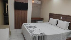 a bedroom with a bed with white sheets and a television at Hotel pousada a Cabana in Maceió