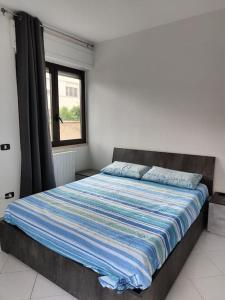 a bedroom with a bed with a blue striped comforter and a window at Casa Trezza 3 in Latina