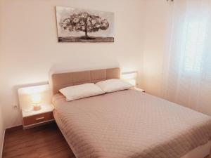 a bedroom with a bed and a tree on the wall at Apartments Nikola Caska in Novalja