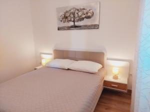a bedroom with a bed with two lamps and a tree on the wall at Apartments Nikola Caska in Novalja