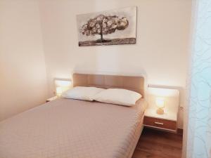 a bedroom with a bed with two lamps and a tree on the wall at Apartments Nikola Caska in Novalja