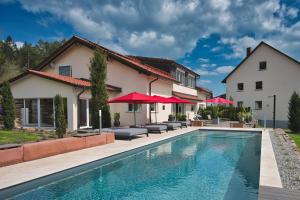 a pool in front of a house with red umbrellas at Romantik Hotel Rindenmühle in Villingen-Schwenningen