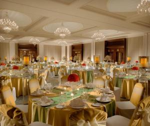 una gran sala de banquetes con mesas, sillas y lámparas de araña en The Leela Palace Chennai en Chennai