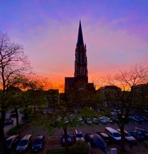 una iglesia con una torre alta y un aparcamiento con coches en “De Koelemert” en Aalst