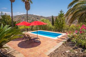 two red umbrellas and chairs next to a swimming pool at Casa Girasol in Torrox