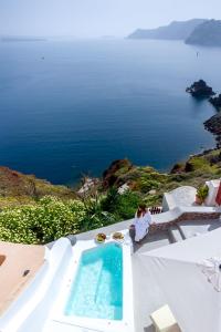 a woman sitting next to a swimming pool with a view of the ocean at Cleo's Dream Villa in Oia