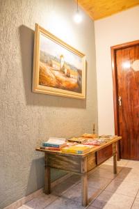 einen Holztisch mit Büchern an einer Wand mit einem Gemälde in der Unterkunft POUSADA GIRASSOL in Santo Antônio do Pinhal
