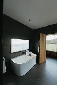 uma grande banheira branca numa casa de banho preta com uma janela em CABN Kangaroo Island em Penneshaw