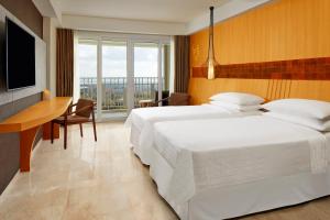 two beds in a hotel room with a desk and a television at Four Points by Sheraton Bali, Ungasan in Jimbaran