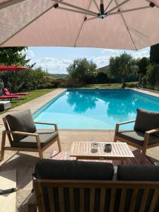 uma piscina com duas cadeiras, uma mesa e um guarda-sol em Chambres d'hôtes de charme La Joséline em Flayosc