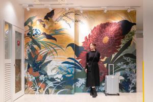 a woman standing in front of a wall with a flower mural at Hotel Sanrriott Osaka Hommachi in Osaka
