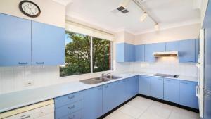 une cuisine avec des placards bleus et une horloge murale dans l'établissement Sanctuary #12 Accom Holidays, à Terrigal