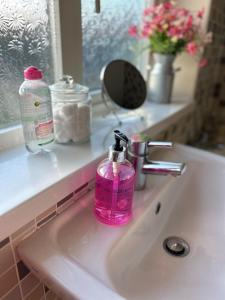 a pink bottle of soap sitting on a bathroom sink at Modern 3 bed house 2 parking spaces contractors welcome in Stevenage