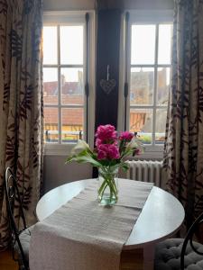 eine Vase rosafarbener Blumen auf einem Tisch vor den Fenstern in der Unterkunft La petite duchesse in Vernon