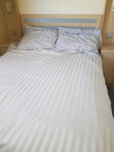 a white bed with striped sheets and pillows at 6 berth holiday home on Ocean Edge near Morecambe in Heysham