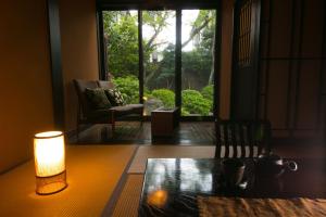 a table with a lamp and a chair and a window at Bettei Haruki in Beppu