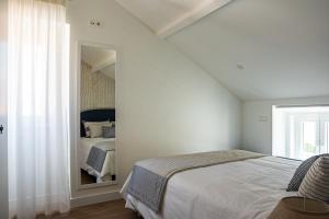 een witte slaapkamer met een bed en een spiegel bij Casa Ribeiro in Nazaré