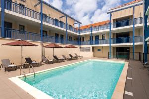 - une piscine en face d'un bâtiment avec des chaises et des parasols dans l'établissement Lagrange Vacances Les Balcons de l'Océan, à Biscarrosse