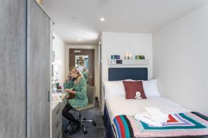 una donna seduta a una scrivania in una stanza con un letto di For Students Only Ensuite Bedrooms with Shared Kitchen at Reynard House located in Leicester a Leicester