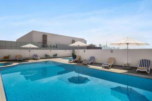 una piscina con sillas y sombrillas en un edificio en La Quinta by Wyndham Dubai Jumeirah, en Dubái