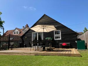 a house with a deck with a table and an umbrella at Lime Tree Cottage in Tillingham
