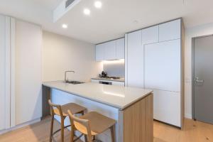 a kitchen with white cabinets and a counter with two chairs at ULTIQA Signature at Broadbeach in Gold Coast
