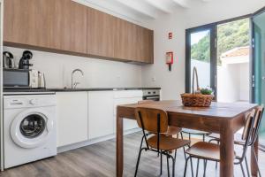 a kitchen with a wooden table and chairs and a washing machine at Encanto Village House in Faial da Terra
