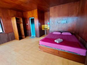 ein Schlafzimmer mit einem rosa Bett in einem Holzzimmer in der Unterkunft Derawan Fisheries Cottage in Derawan Islands