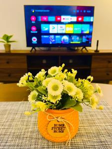 un jarrón de flores amarillas sobre una mesa con TV en P1 PineComfyStay Waterpark 7pax Ipoh en Kampong Pinji