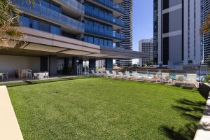 a lawn in front of a building with chairs and a pool at ULTIQA Signature at Broadbeach in Gold Coast