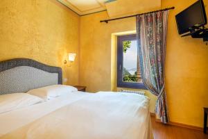 1 dormitorio con cama blanca y ventana en La Griglia Hotel, en Argegno