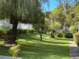 una panchina da parco seduta sull'erba sotto un albero di Parkline Apartments Perth a Perth